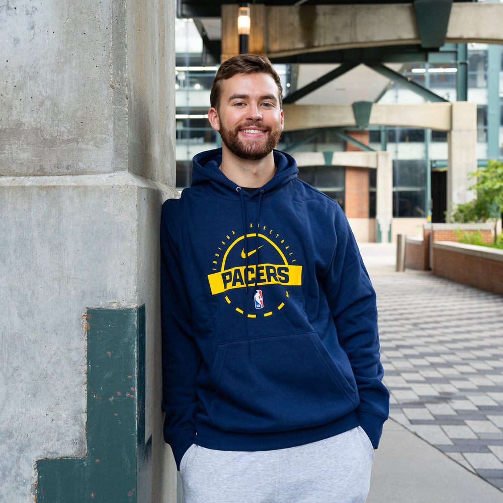 Man wearing a Pacers hoodie leaning against a wall outdoors.